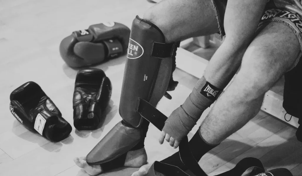 Muay Thai student removing gear and shin guards after training in Toronto.